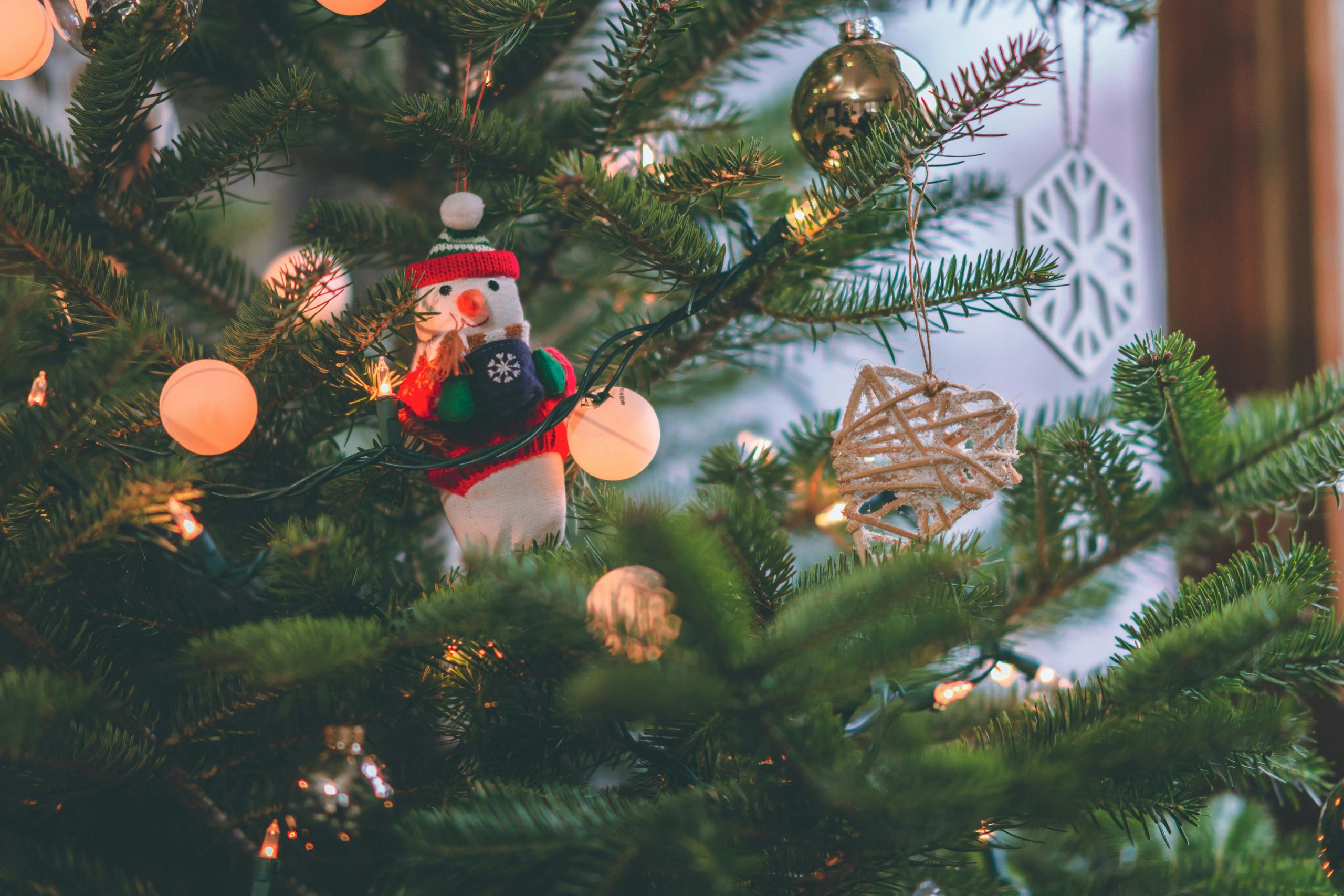 Close-up of a decorated Christmas tree featuring a snowman ornament and glowing lights.