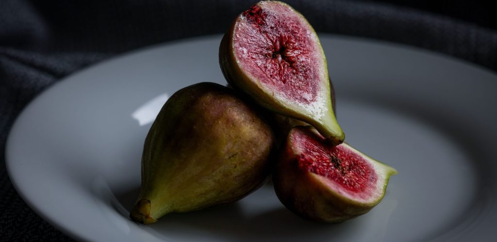 Fresh figs sliced open, displayed on a plate against a dark textured background.
